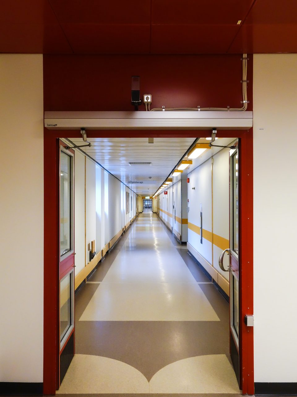 Hospital corridor seen through a set of red-framed cross-corridor doors held open at Norra Älvsborg County Hospital in Sweden